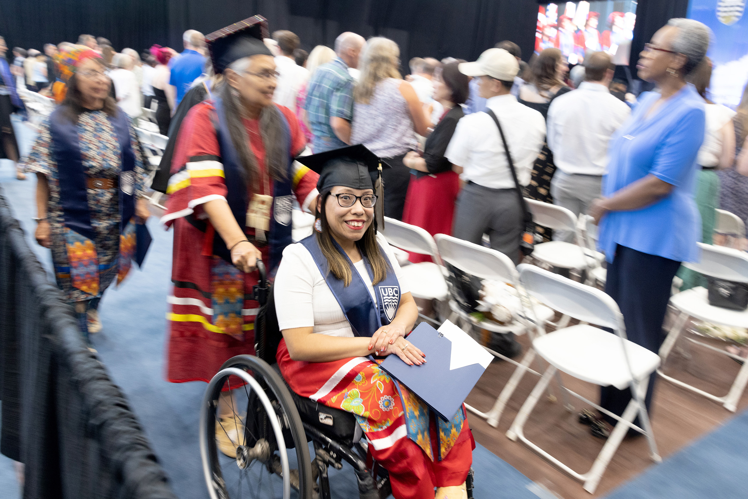 Woman on wheelchair moves through audience at graduation ceremony