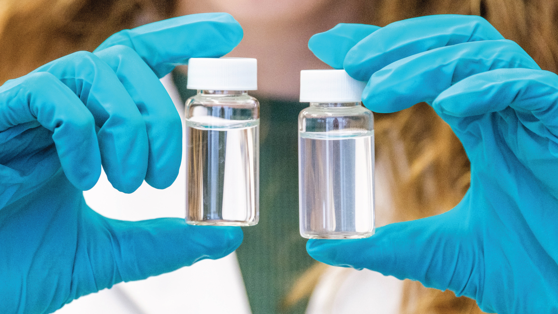 Person wearing gloves holding two small clear containers of liquid