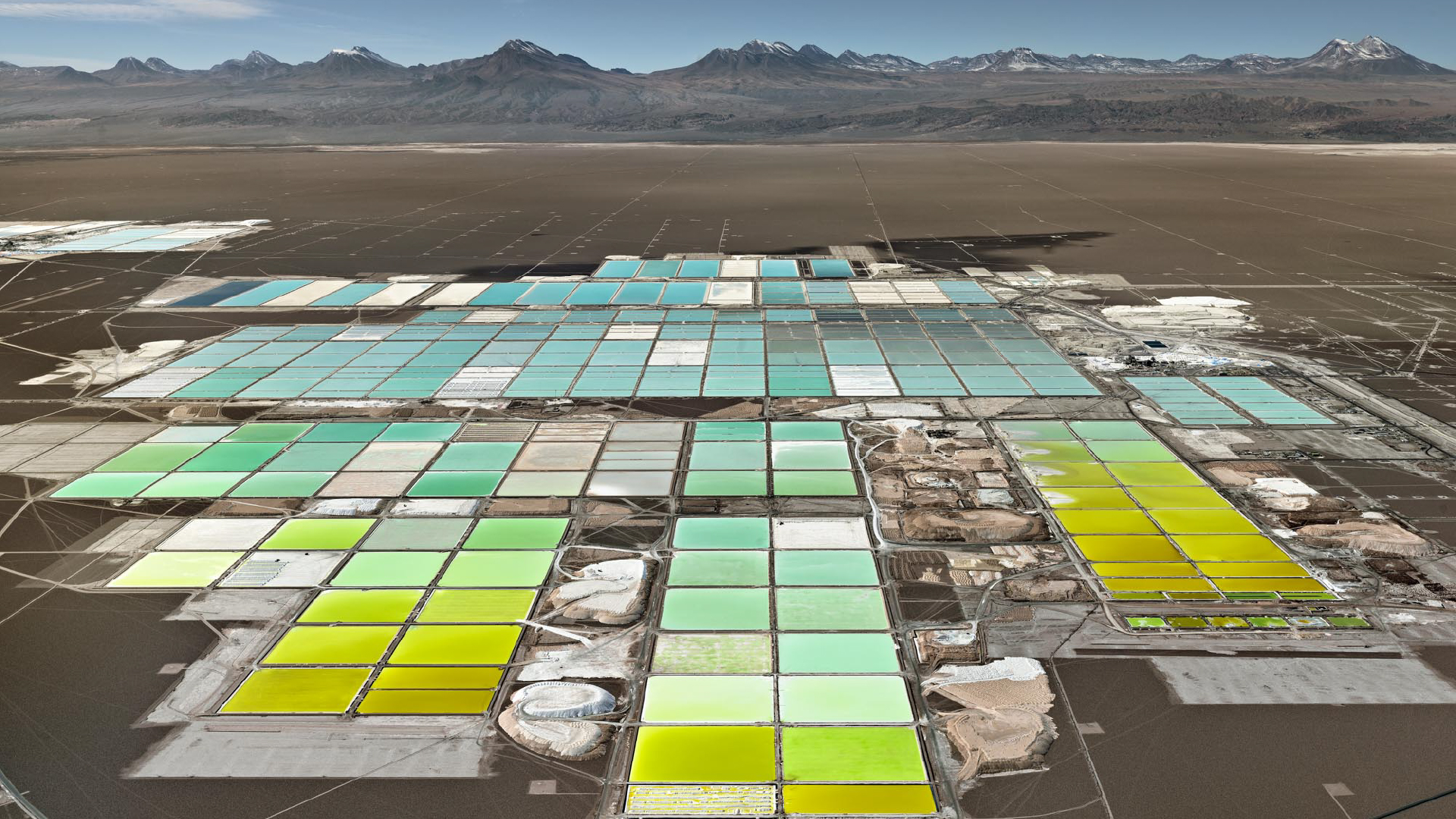 An aerial view of lithium mines: rectangular pools of greens, blues, and yellows