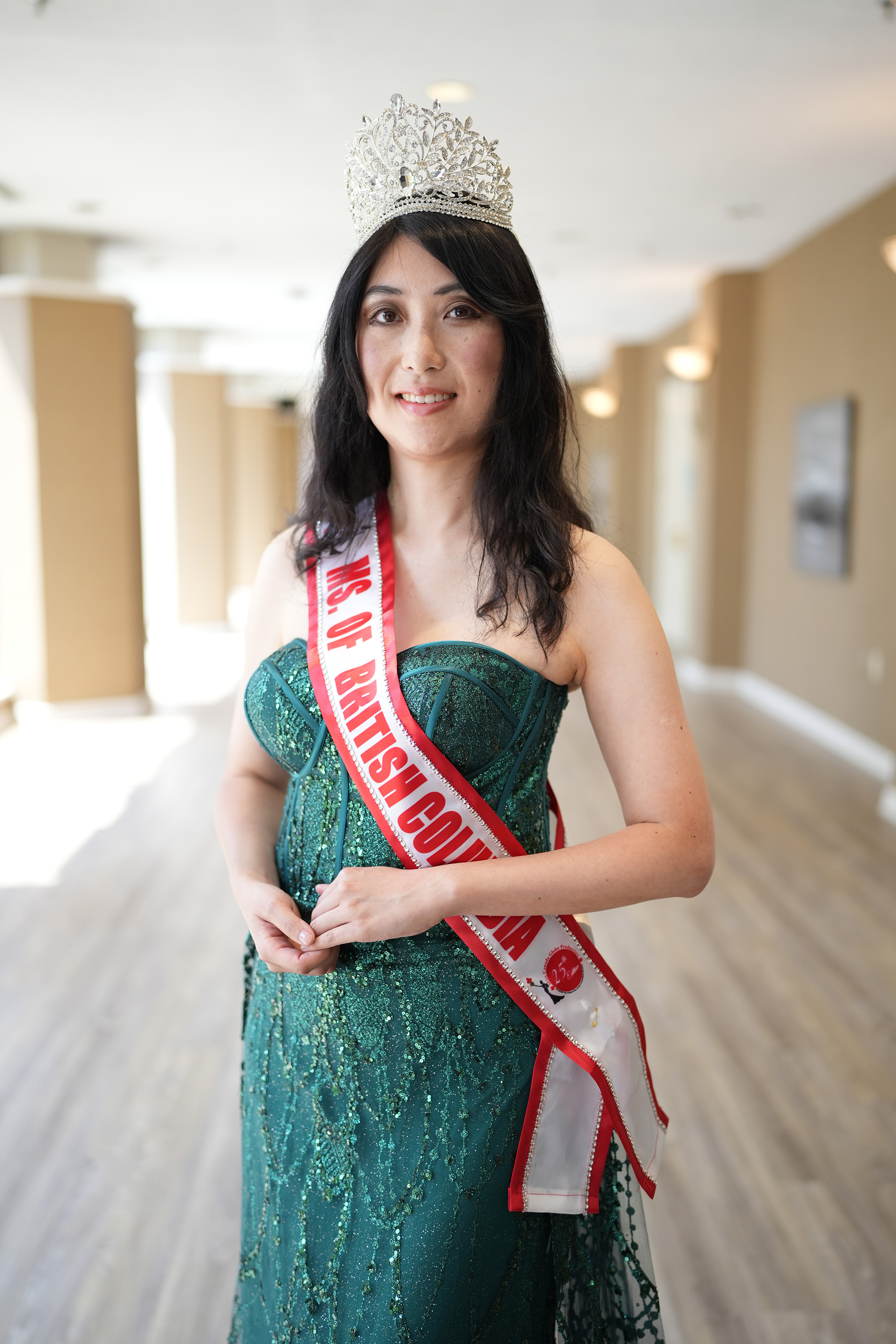 A photo of Wendy Leung posing while wearing a green dress, red and white sash, and crown.