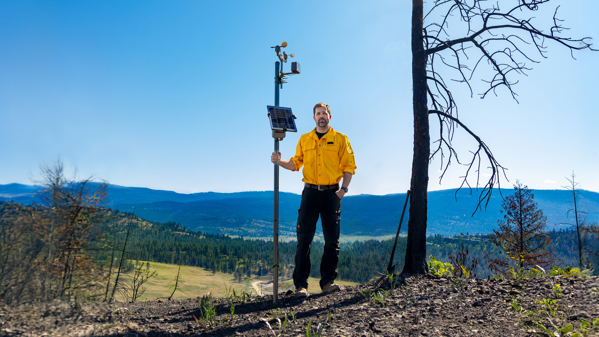 Man stands holding pole with attached devices overlooking valley