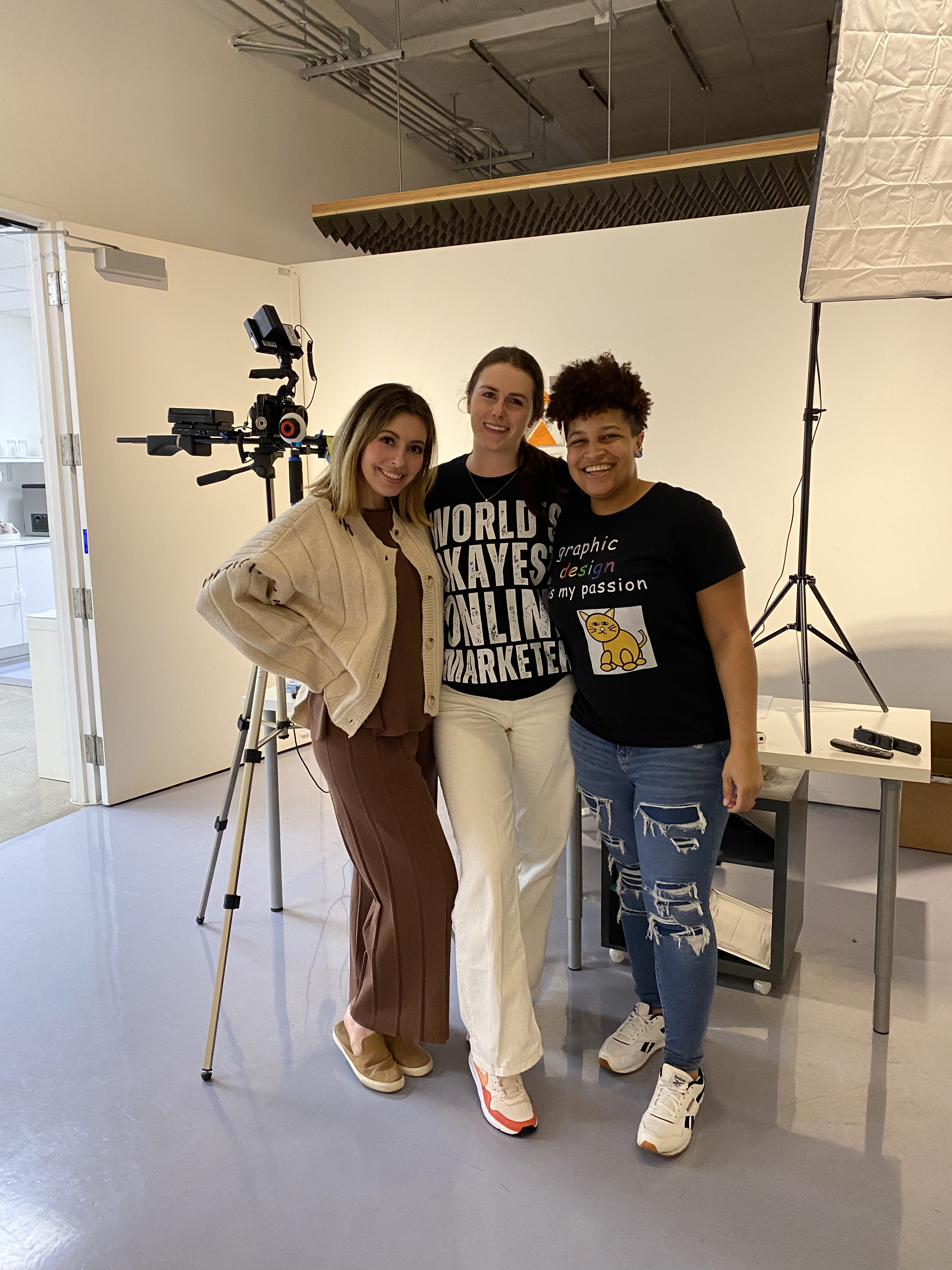 Three people posing together in front of camera equipment.  One of them is Kortnee Paiha.