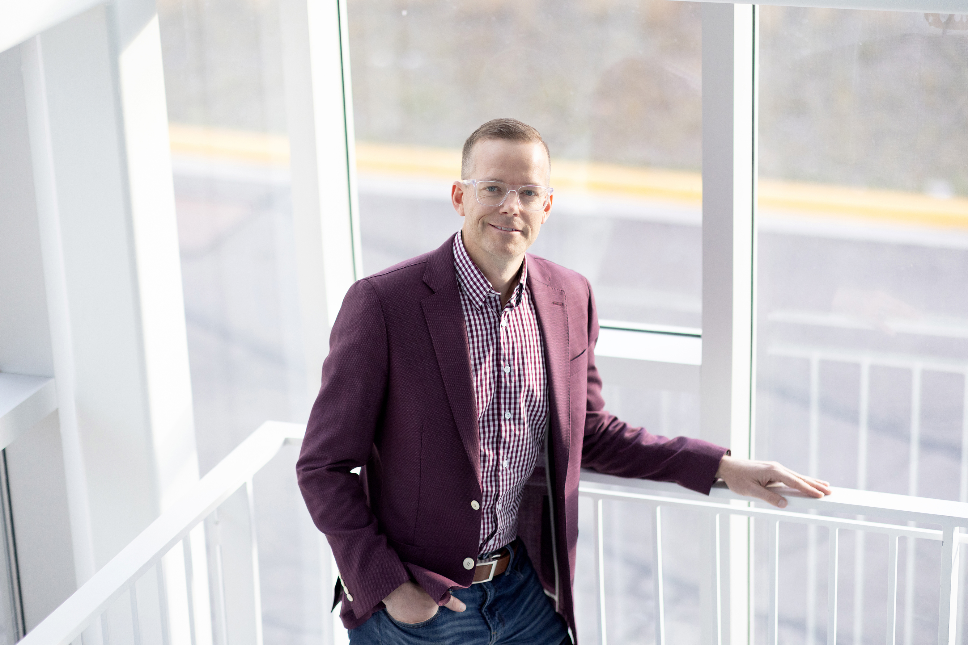 Man with glasses stands against railing in front of windows