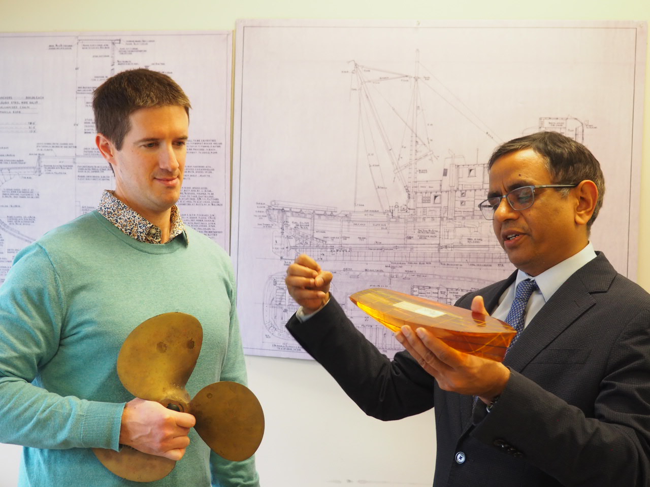 Two researchers look at ship model, while one holds propeller model