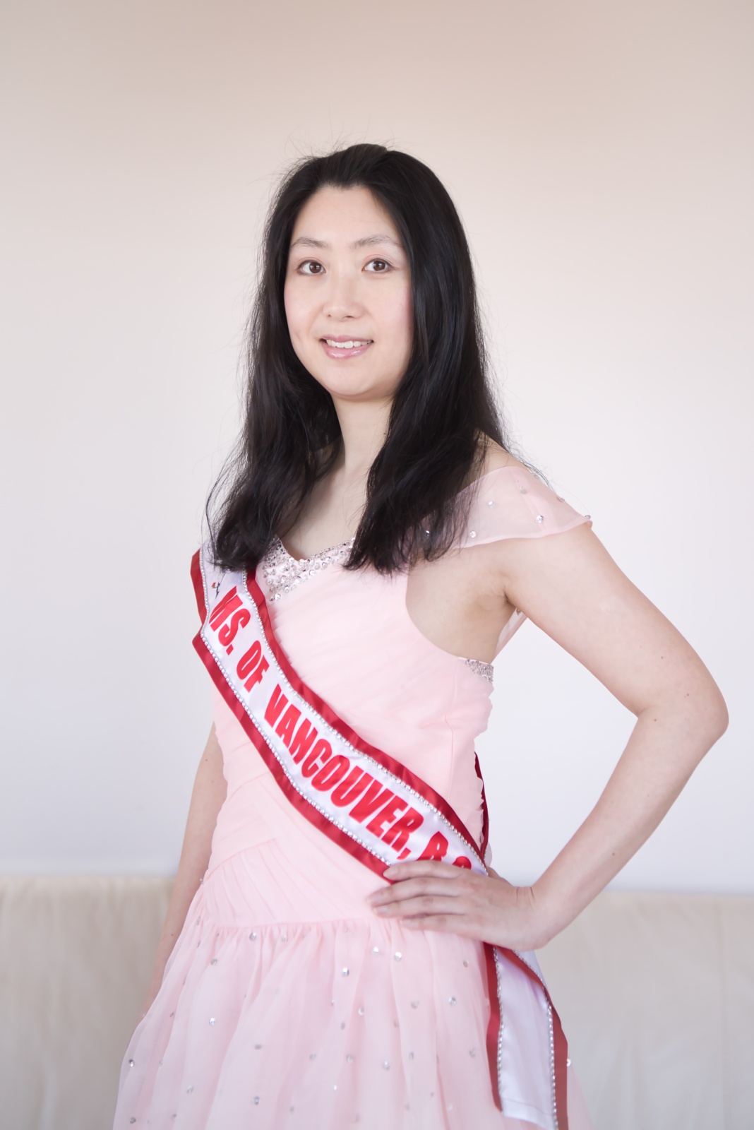 A photo of Wendy Leung posing while wearing a pale pink dress and red and white sash.