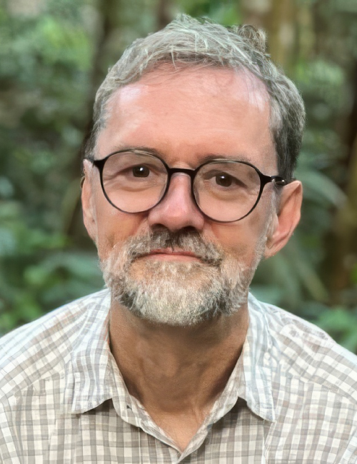 A headshot of Philip Holden with short salt and pepper hair, black glasses, and a collared shirt.