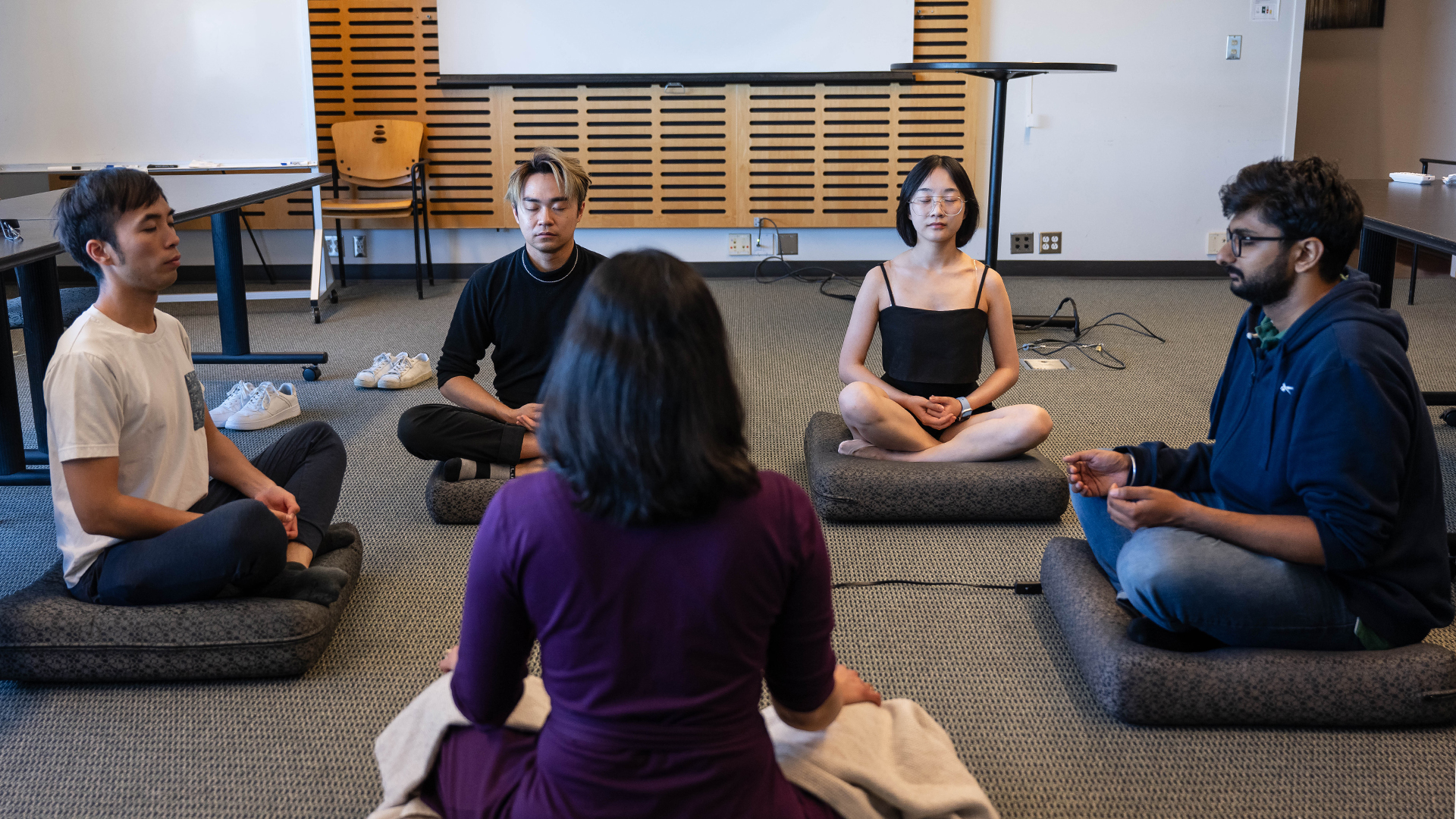 Dr. Verada Kolhatkar leads a meditation with a group of students — all are seated on the floor, cross-legged in a circle