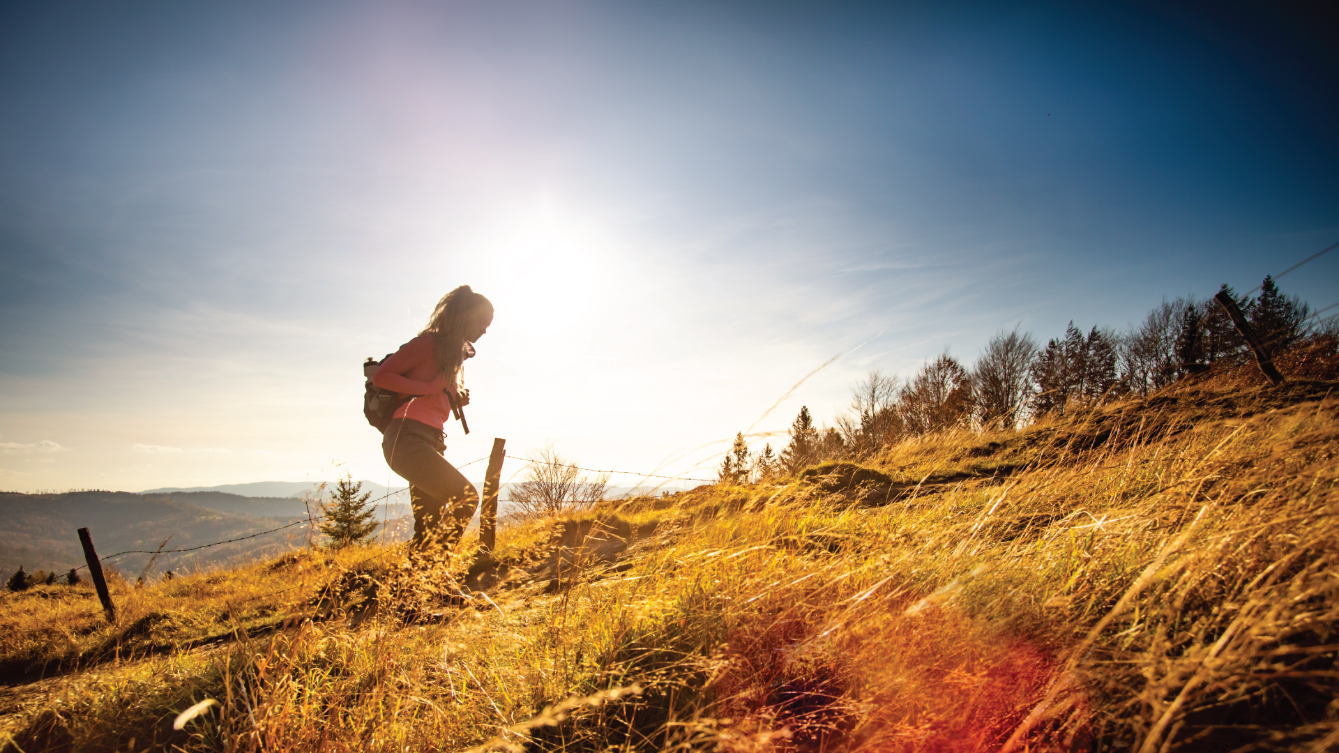 A person hikes a grassy uphill trail