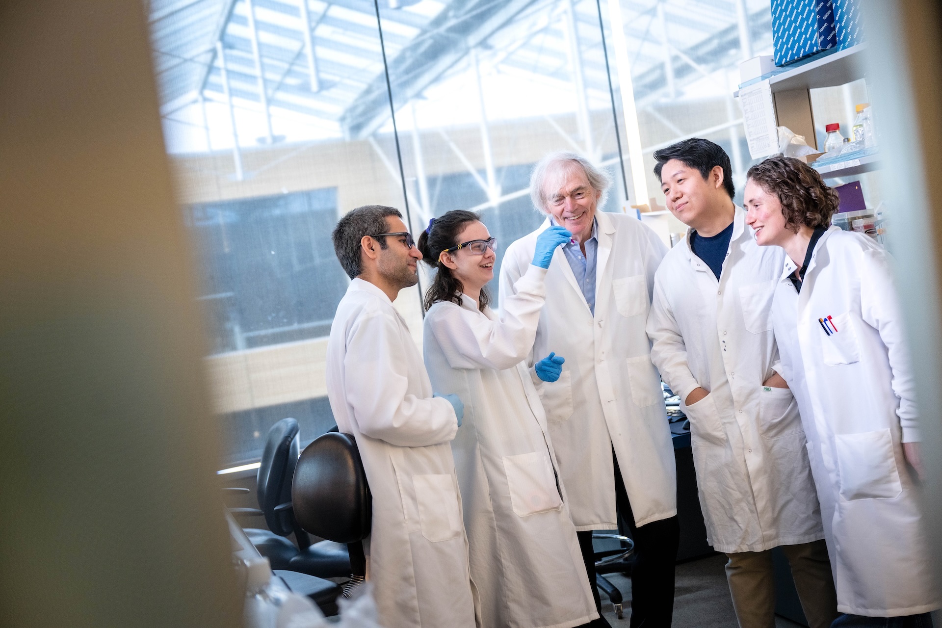 Five people in lab coats smile while looking at vial