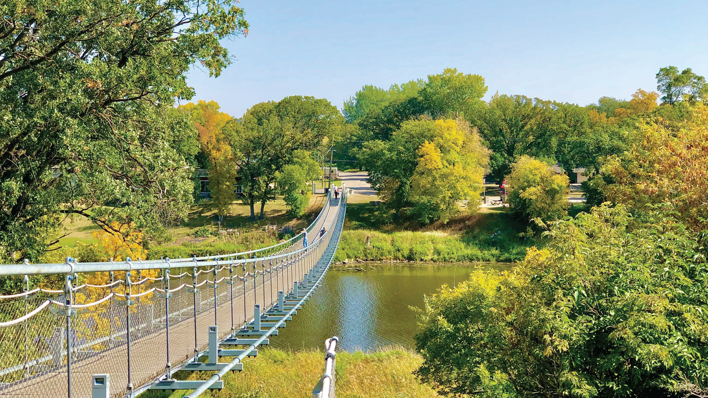 A low suspension bridge above a river surrounded by deciduous trees