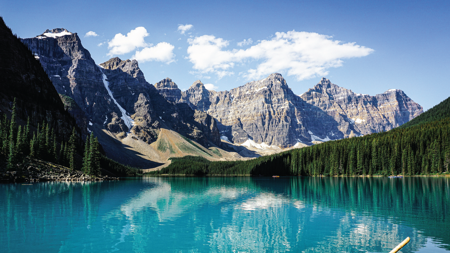 A turquoise lake surrounded by evergreen forest and several jagged grey peaks