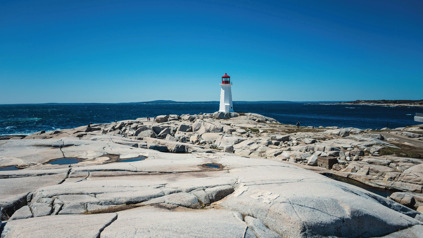 A white lighthouse with red lantern room on a rocky outcropping