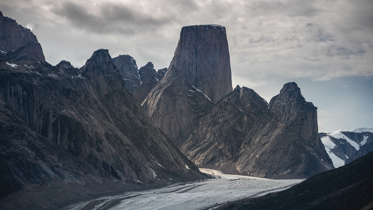 A flat-topped mountain surrounded by jagged grey peaks with snow on the ground