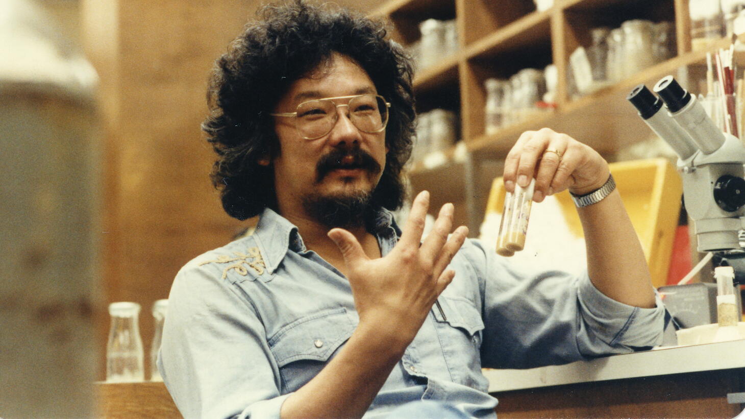 A man with long hair and clear aviators sits in a lab