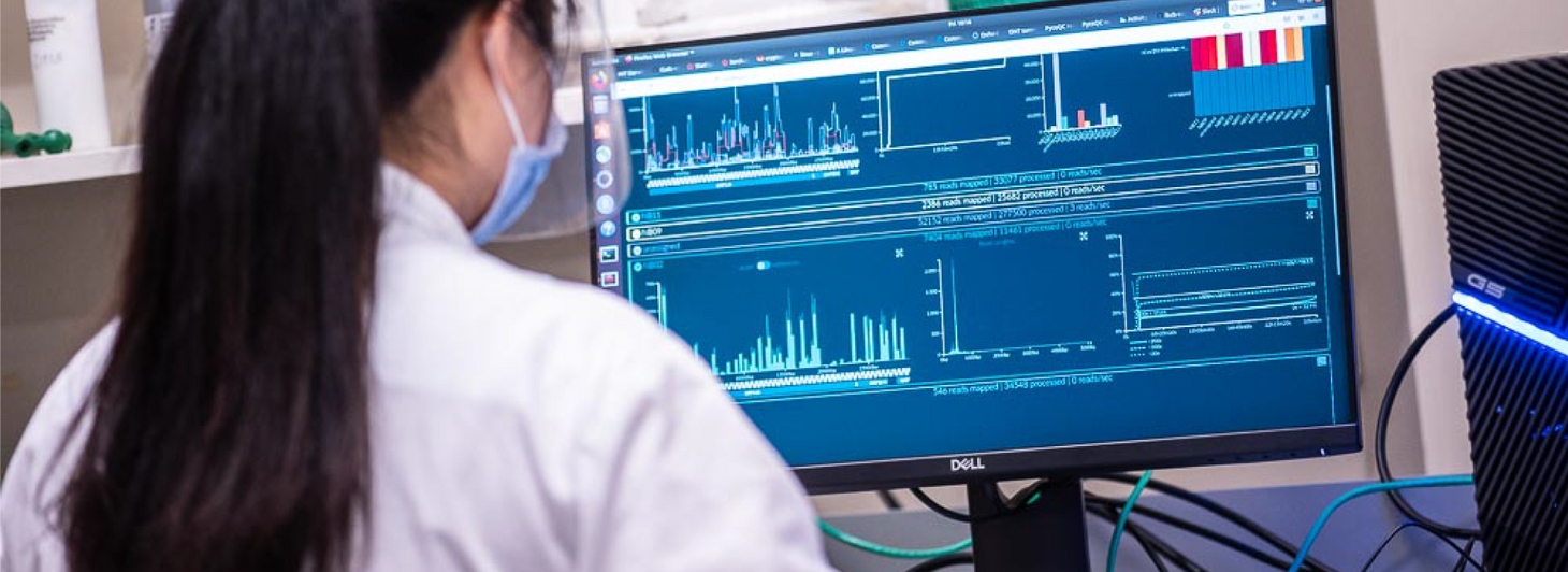 Woman in PPE and lab coat analyzes data on computer screen