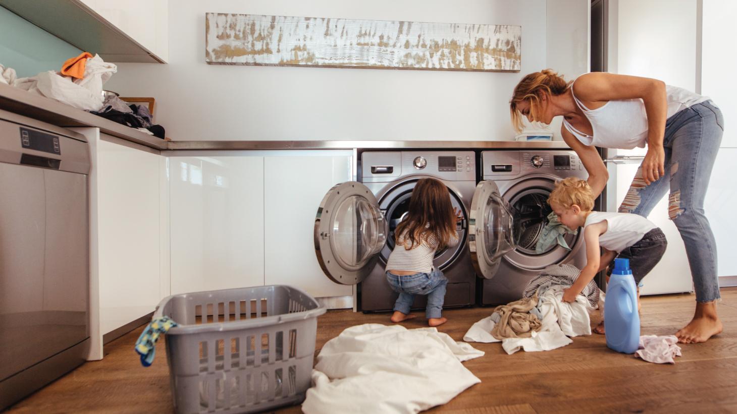 A woman and two kids putting clothes into a laundry machine