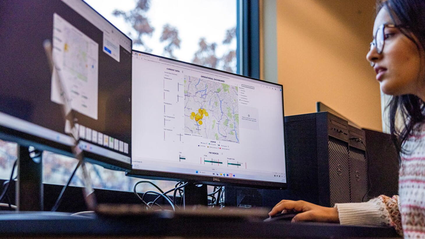 Undergraduate student Saxena reviews the dashboard of a wildfire sensor project on dual monitor screens.