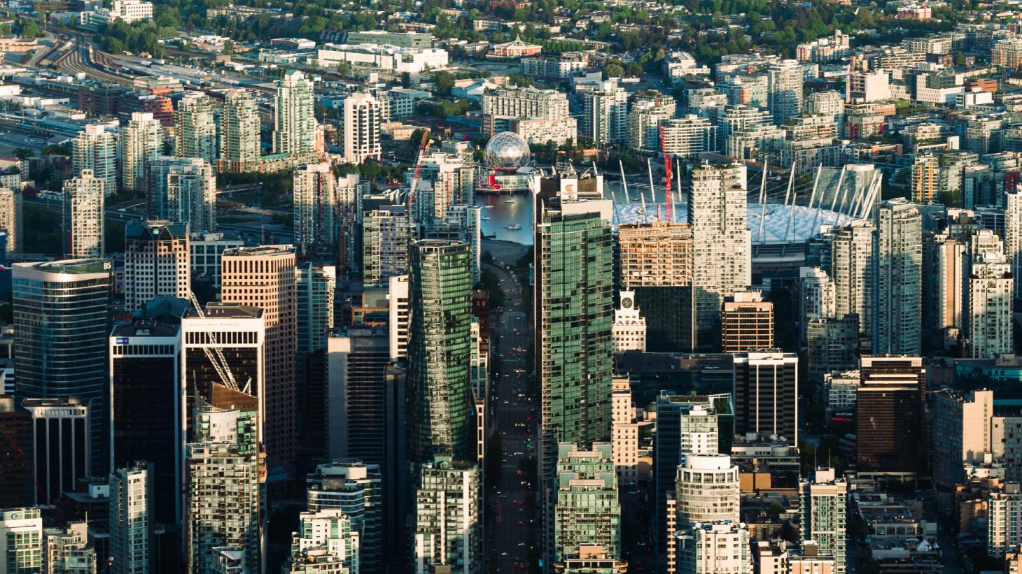 A photograph of Vancouver taken from a helicopter above the Stanley Park area. It shows West Georgia Street, with False Creek and Science World at the end, and East Vancouver in the background.
