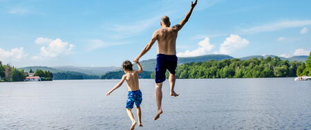A man and a boy jump off of a deck into a lake