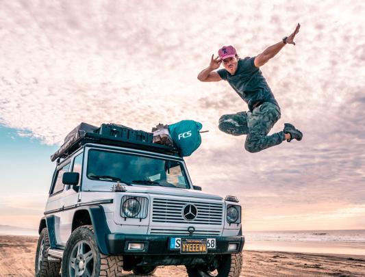 Cole Walliser jumping in mid-air, on a beach in LA, with a jeep in the background