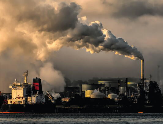 Large plume of smoke from factory complex expands across sky