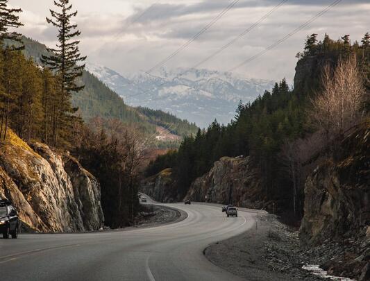 Two cars drive along highway winding through mountainous forest 