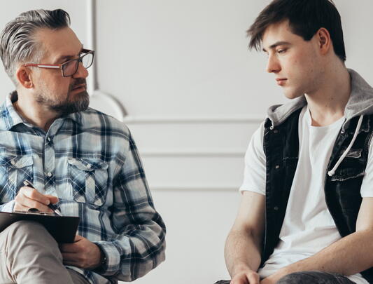 Male therapist with clipboard listening to young man