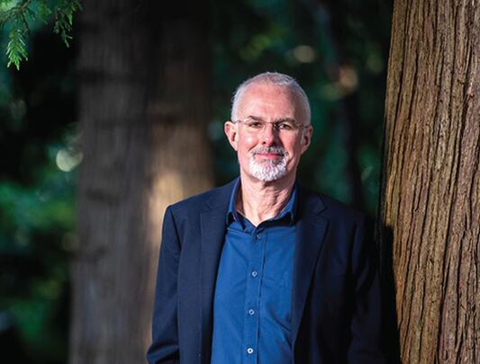 Man in sports jacket standing by tree in forest