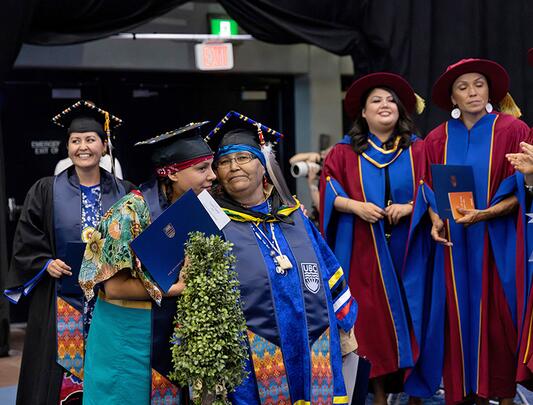 Six women on graduation stage in university regalia