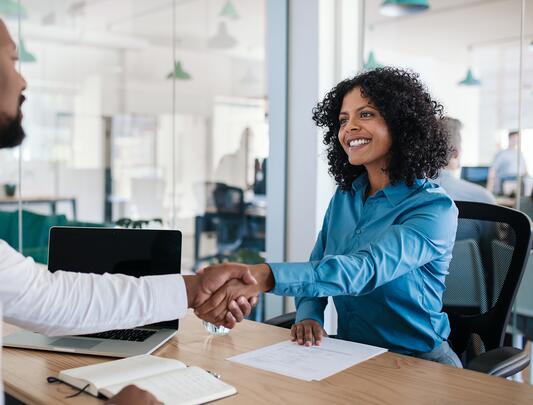 Woman at a desk shaking hands with a man seated across from her