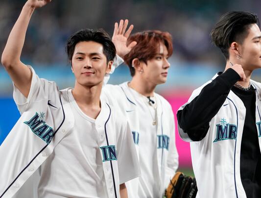 Three Asian young men in baseball jerseys wave at crowd