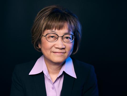 A headshot of Dr. Teresa Tsang with black glasses, short brown hair, and a purple collared shirt.