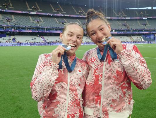 Two female Canadian Olympic athletes on the field showing their silver medals