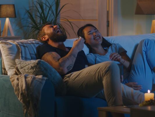 Man and woman laughing on couch in front of TV screen