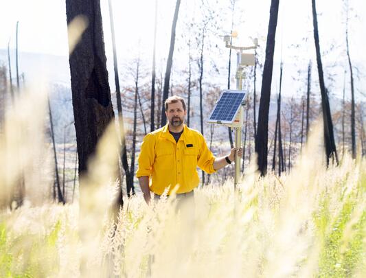 Man standing in field holding pole with devices attached