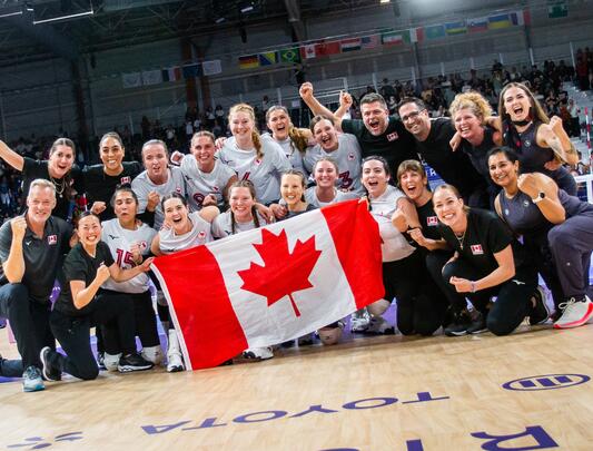 Athletic team cheering and holding Canadian flag in a gym