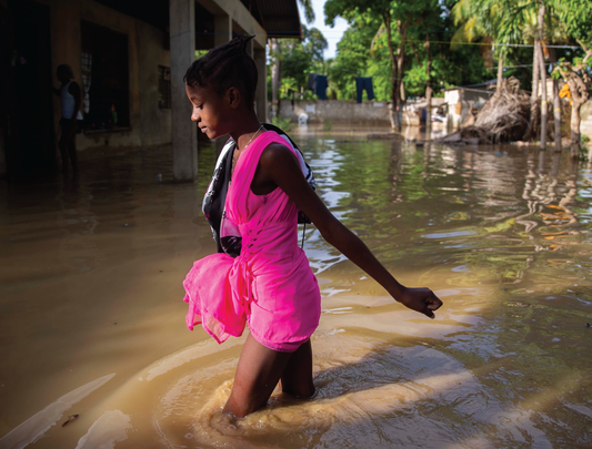 Girl in pink outfit wades through flood water in Haiti