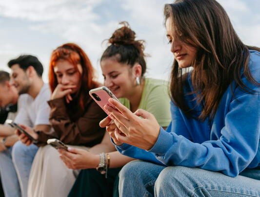 Young people sitting in a row outside looking at smartphones