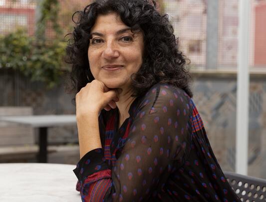 A portrait of Meeru Dhalwala with curly black hair and her chin propped in her hand.