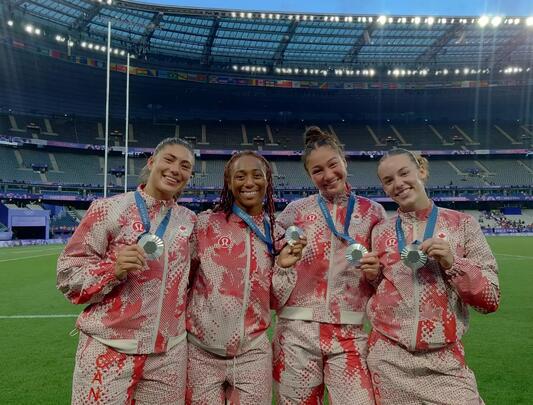 Four women athletes stand on field with their Olympic medals