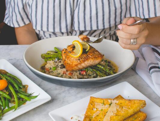 Person eating plate of salmon on asparagus and rice at table
