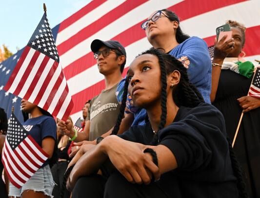 Supporters of Vice President Kamala Harris during her concession speech for the 2024 presidential election, with American flags in the background 