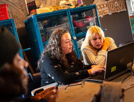 Two people seated at a table, looking at a laptop screen