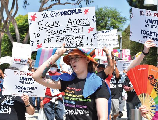Protestors holding signs and displaying Pride rainbows