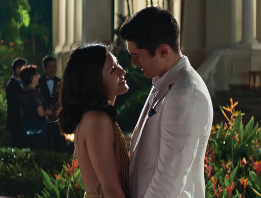 Asian woman and man in evening wear lean into a kiss