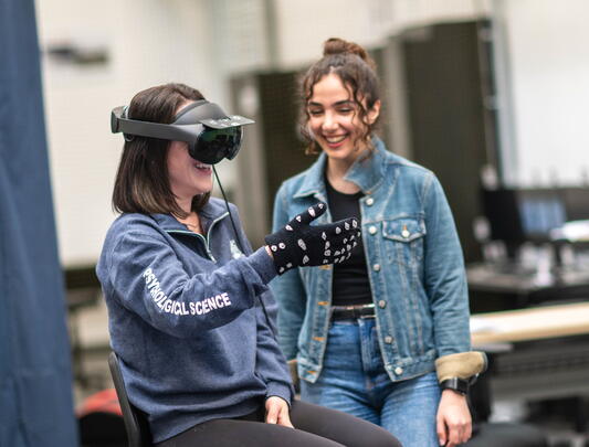 Woman wears VR headset and gloves as another woman watches 