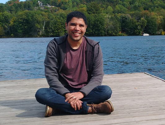 Hugo Mota Santos seated on a deck with water and trees in the background