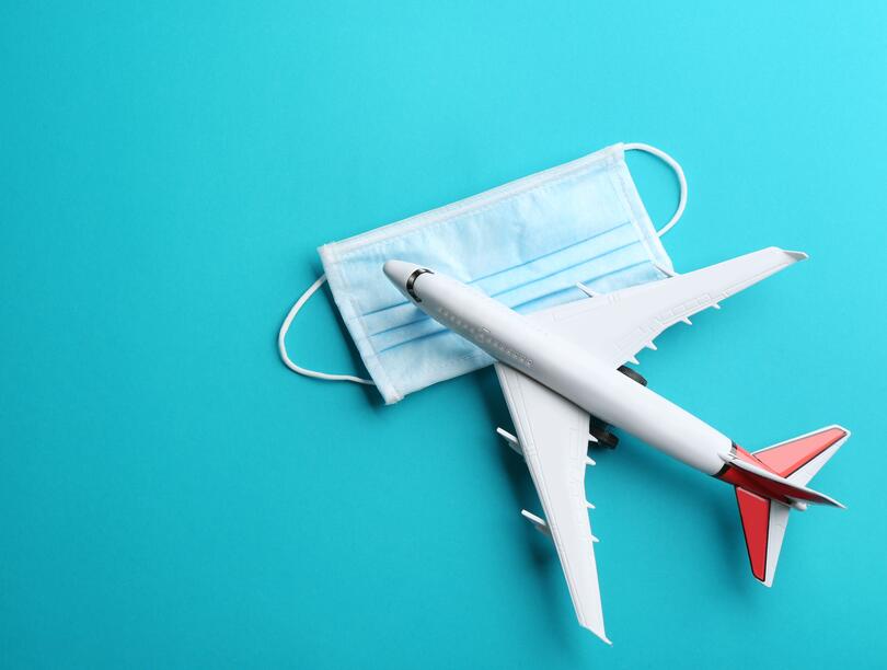 Toy airplane and protective mask on light blue background, flat lay with space for text. Travelling during coronavirus pandemic