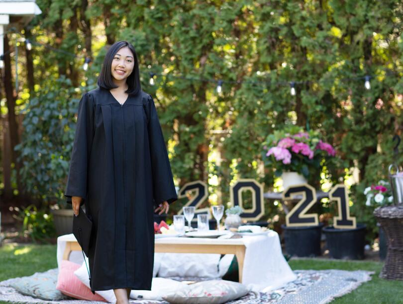 Student in graduation gown at an outdoor celebration with 2021 sign in background