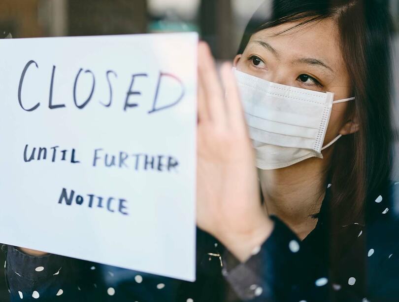 A masked woman puts up a closed sign on a shop.